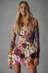 Woman wearing a sheer mini dress with 3D floral appliqués in various colors.