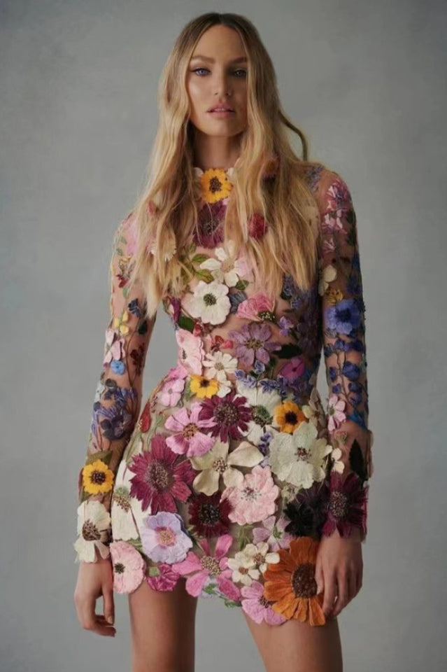 Woman wearing a sheer mini dress with 3D floral appliqués in various colors.
