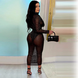 back view of a woman in a sheer black long-sleeved dress with a plunging neckline and a high slit, holding a black clutch bag and wearing black strappy heels