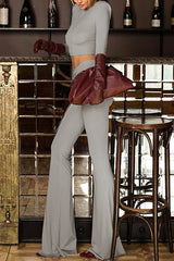 Side view of a woman in a gray cropped long-sleeve top and gray flare pants, holding a burgundy clutch bag and wearing burgundy gloves.