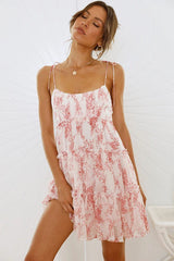 Woman wearing a white and pink floral print mini dress with spaghetti straps and ruffles.