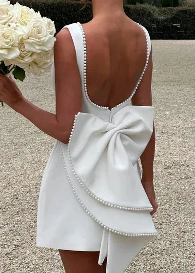 woman holding a bouquet of white roses, wearing a white dress with a large bow