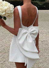 woman holding a bouquet of white roses, wearing a white dress with a large bow