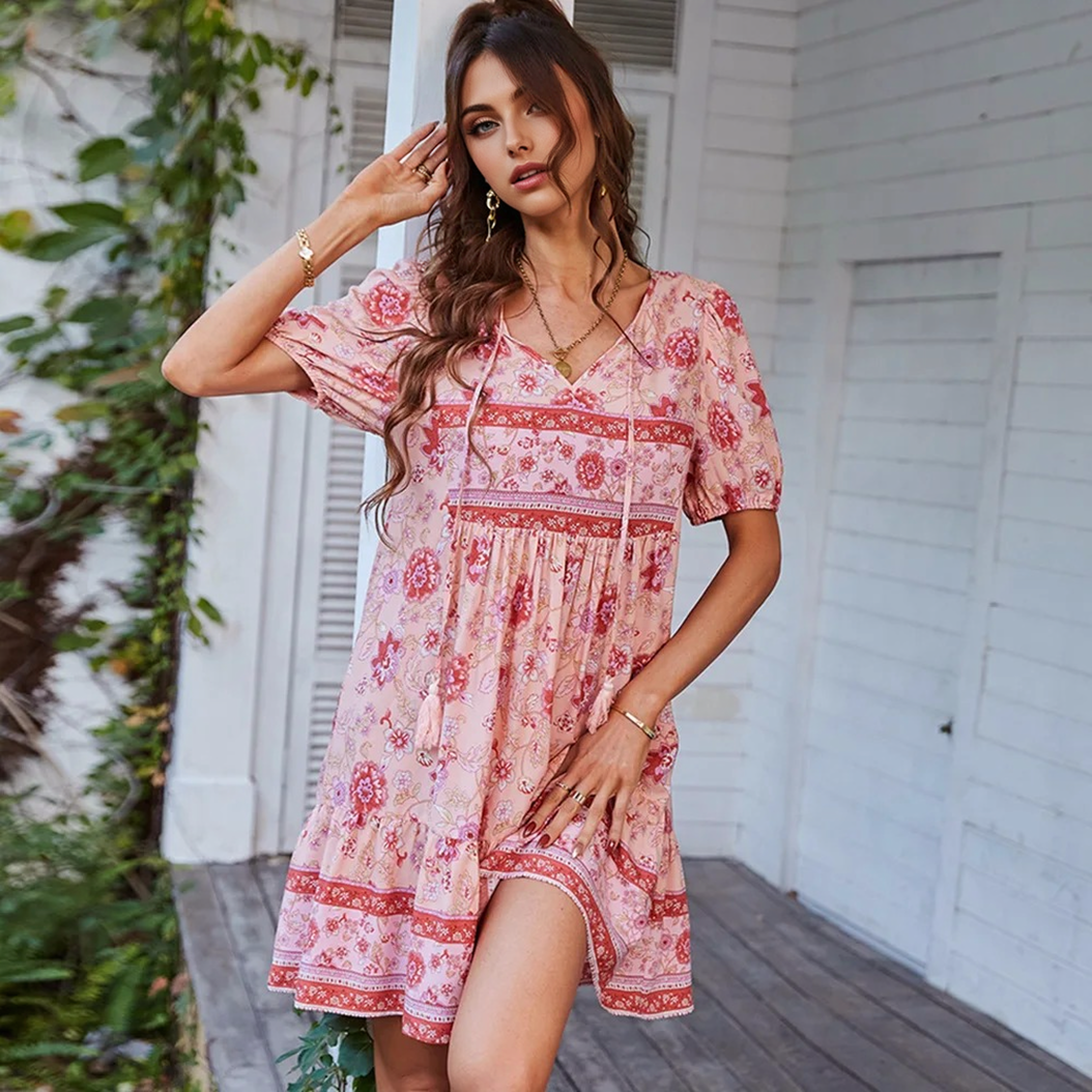 Woman posing in a pink floral print mini dress with puff sleeves and a tie neck