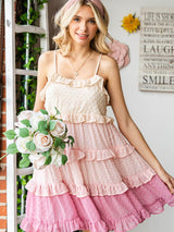 A young woman smiling and holding a bouquet of flowers, wearing a pink and beige ruffled dress with a swiss dot pattern.