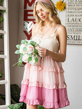 A young woman looking down at a bouquet of flowers, wearing a pink and beige ruffled dress with a swiss dot pattern.