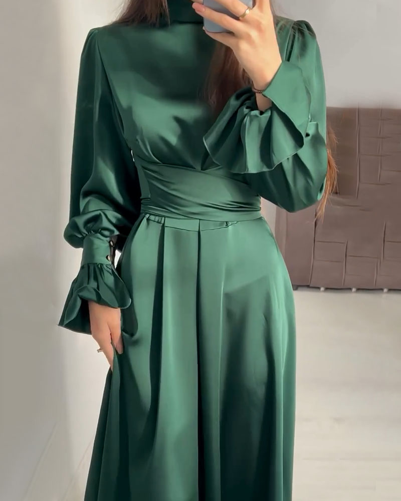 Close-up of a woman wearing an emerald green satin dress, focusing on the cinched waist and ruffled cuffs.