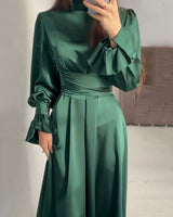 Close-up of a woman wearing an emerald green satin dress, focusing on the cinched waist and ruffled cuffs.