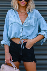 Woman wearing a light blue cropped denim shirt with black distressed shorts and a beige handbag.