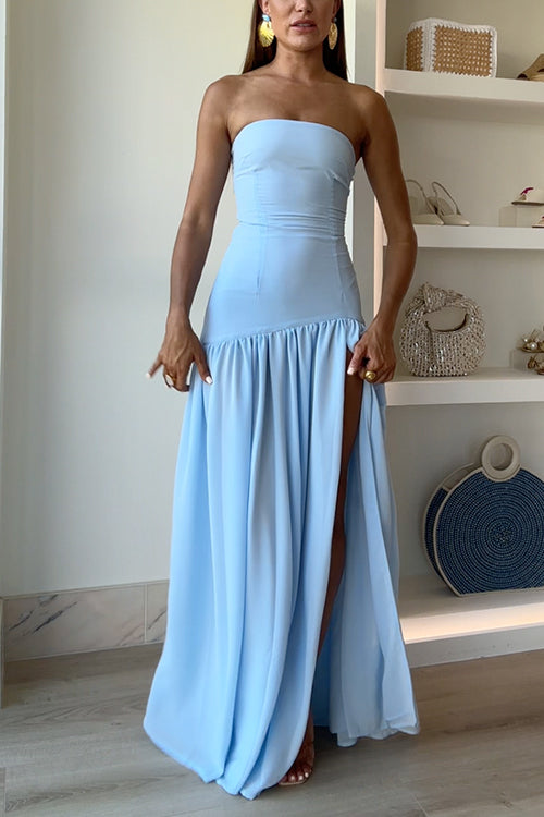 A woman poses in a light blue strapless maxi dress with a high slit.