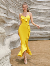 A model wearing a bright yellow bodycon dress with a ruffled hem and spaghetti straps, posing outdoors in front of a rocky formation.