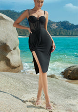 Full body shot of a woman in a black corset dress with a high slit on a beach.