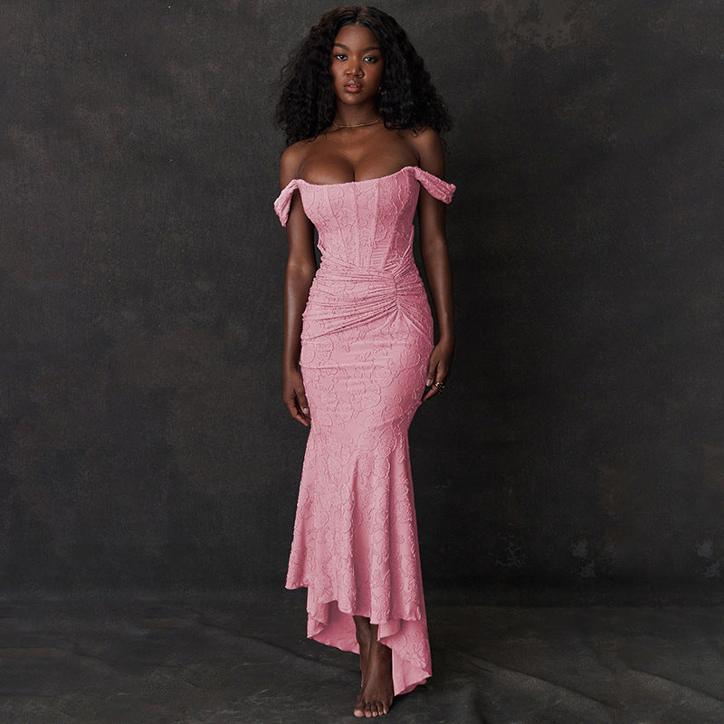 A Black woman models a pink off-the-shoulder ruched mermaid gown with a high-low hemline.