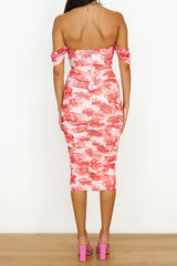 back view of a woman in a pink and red floral print off-the-shoulder ruched midi dress and pink strappy heels