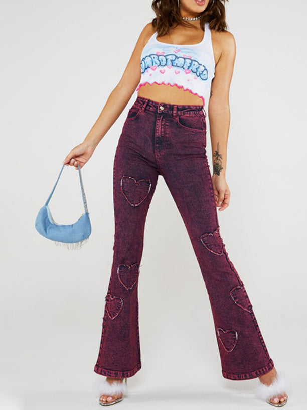 A woman wearing a white halter neck crop top with a blue and pink graphic print and pink hearts, paired with purple acid wash flare jeans with heart cutouts.