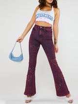 A woman wearing a white halter neck crop top with a blue and pink graphic print and pink hearts, paired with purple acid wash flare jeans with heart cutouts.