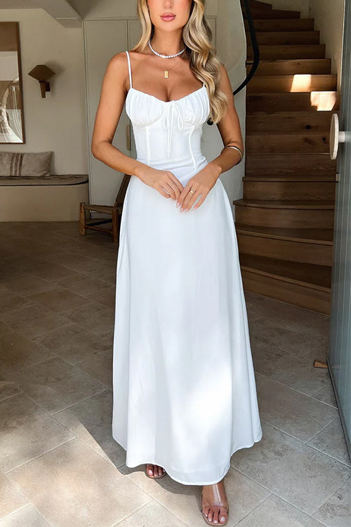 A woman in a white maxi dress with spaghetti straps and a tie-front bodice, standing indoors.