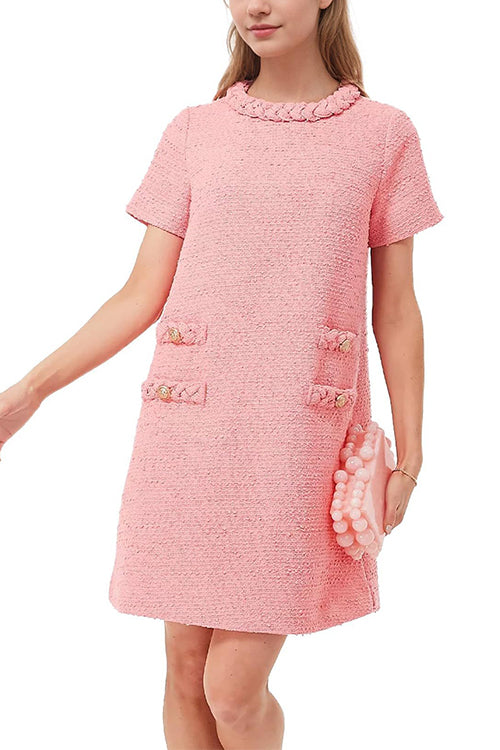 A woman wearing a pink tweed shift dress with short sleeves and decorative pockets, holding a pink beaded clutch.