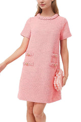 A woman wearing a pink tweed shift dress with short sleeves and decorative pockets, holding a pink beaded clutch.