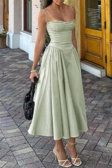 Woman wearing a sage green bustier midi dress with a full pleated skirt and strappy heels, holding a black handbag.