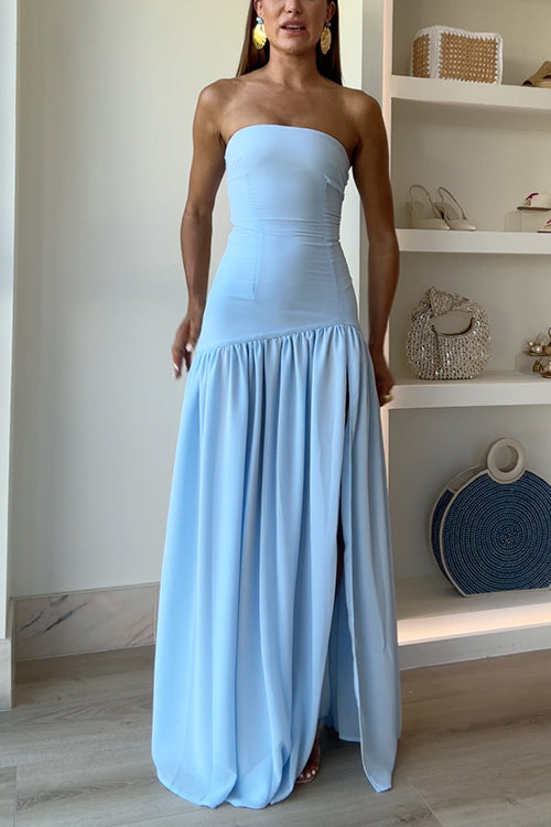 A woman stands in a light blue strapless maxi dress with a high slit.