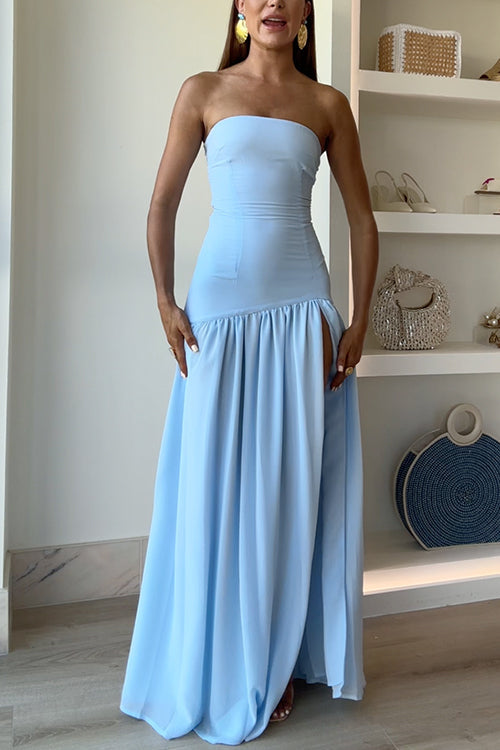 A woman with large gold earrings in a light blue strapless maxi dress with a high slit.