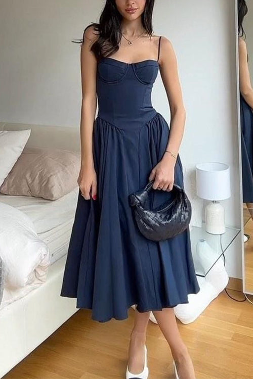 Woman wearing a navy blue bustier midi dress with a full pleated skirt and white heels, holding a black handbag.
