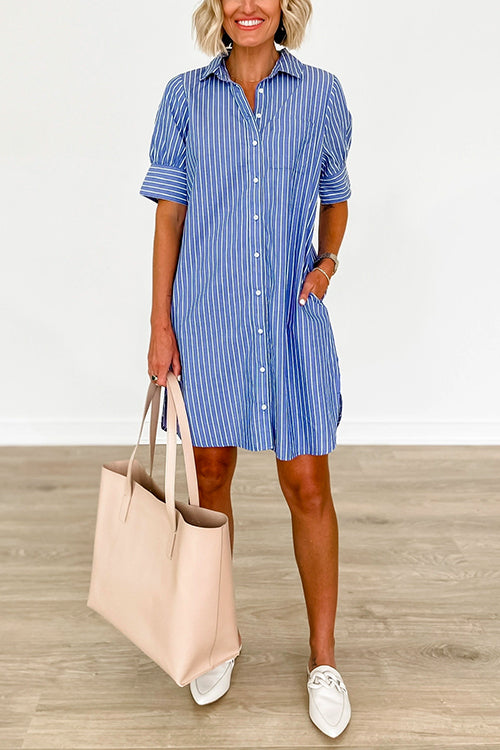 Woman wearing a blue and white striped shirt dress with white loafers and a large beige tote bag.