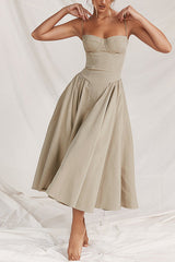 Woman wearing a tan bustier midi dress with a full pleated skirt, posing with hands on hips.
