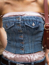 A woman wearing a blue denim strapless corset top with a pink satin trim and a brown bag