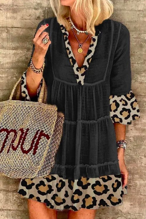 A woman wearing a black tiered dress with leopard print trim and bell sleeves.