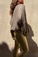 Back view of a woman in a beige oversized knit sweater and gold metallic pants.