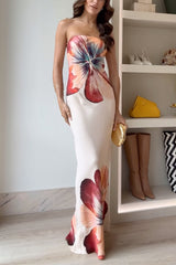 A woman in a cream strapless maxi dress with a large floral print is posing.