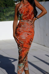 Close-up of a woman modeling an orange and brown tie-dye print ruched halter neck midi dress, focusing on the fabric and ruching.