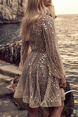 Back view of a woman in a shimmering gold sequined dress with long sleeves.