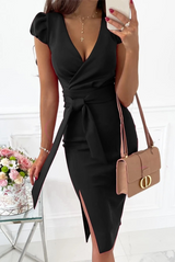 woman wearing a black sheath dress with a v-neck, tie waist, and slit skirt, holding a beige handbag