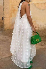 Back view of a woman in a white halter maxi dress with an open back and a green bag.