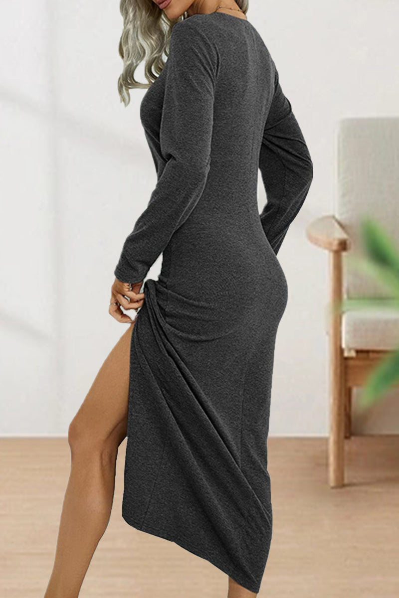 Woman wearing a dark gray long-sleeve dress with a high slit and ruching on the side, her hand lifting the slit.