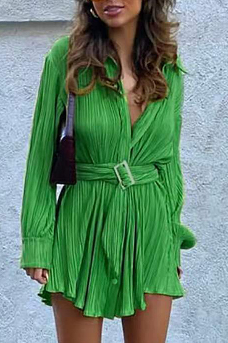 Woman wearing a green pleated long-sleeved shirt dress with a belted waist and black boots.