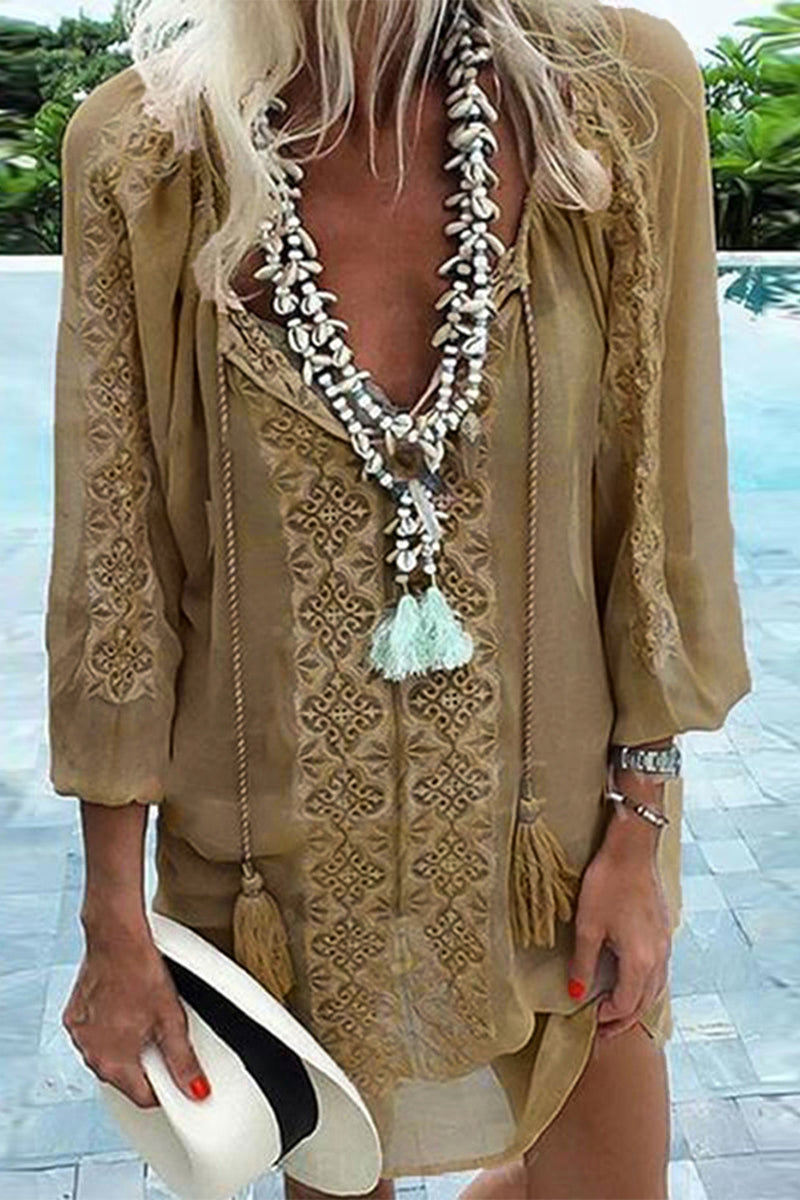 A woman in a tan, flowy tunic holding a white hat.