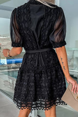 Back view of a woman in a black lace dress with puff sleeves and a belted waist.