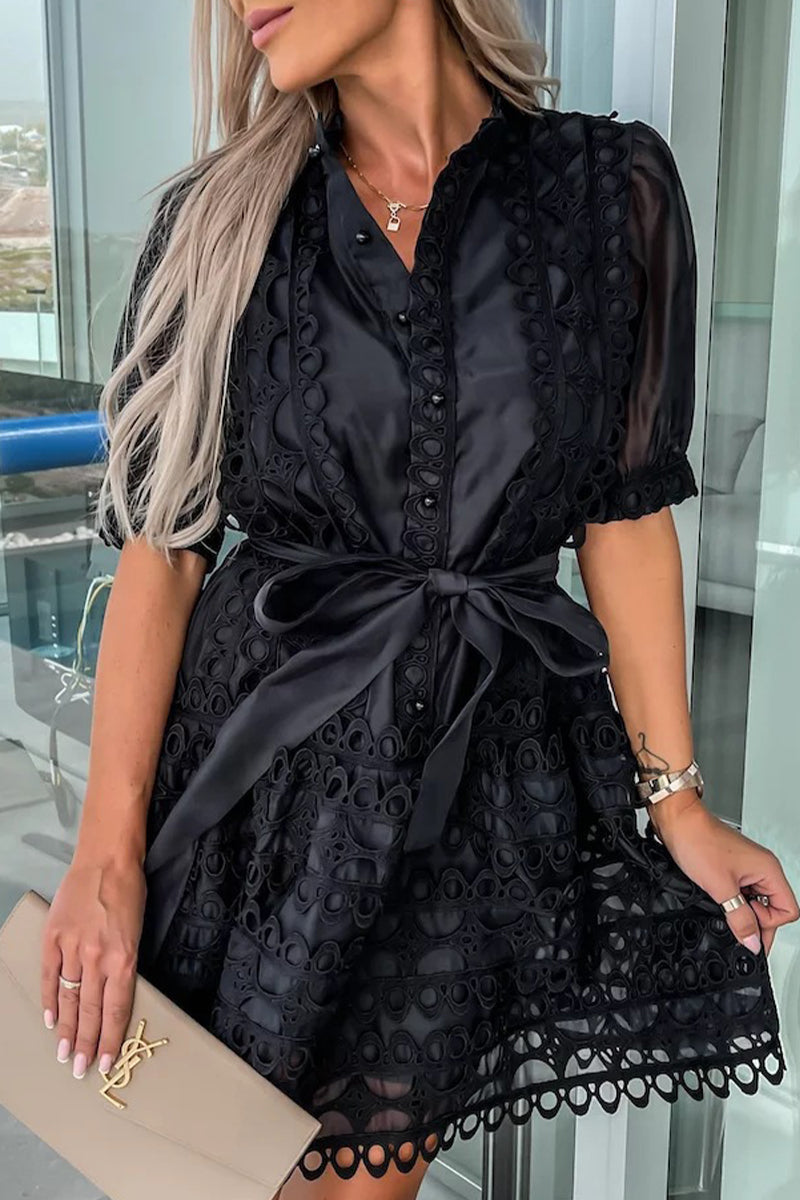 Close-up of a woman wearing a black lace dress with puff sleeves and a belted waist, holding a beige clutch.