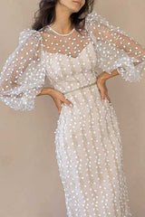 Woman in a cream midi dress with sheer puff sleeves embroidered with white floral motifs and gold accents