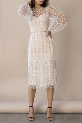 Full body shot of a woman wearing a cream midi dress with sheer sleeves and floral embroidery