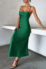 Woman leaning against a white ledge, wearing a green satin slip dress with spaghetti straps and a square neckline.