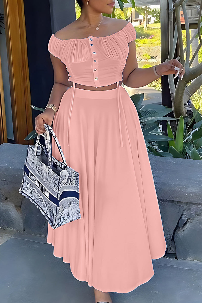 Woman in a pink off-the-shoulder ruched top and wide-leg pants, holding a tote bag.