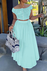 Woman in a mint green off-the-shoulder ruched top and wide-leg pants, holding a tote bag.