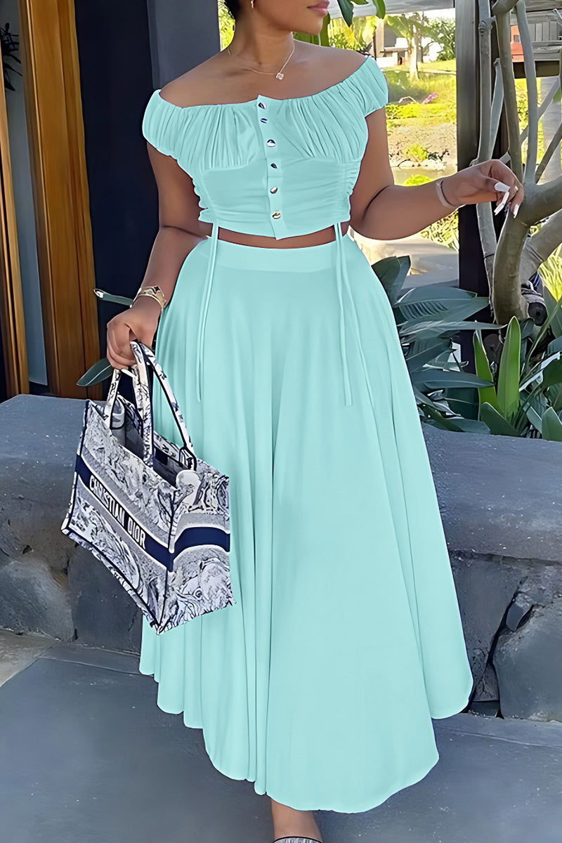 Woman in a mint green off-the-shoulder ruched top and wide-leg pants, holding a tote bag.
