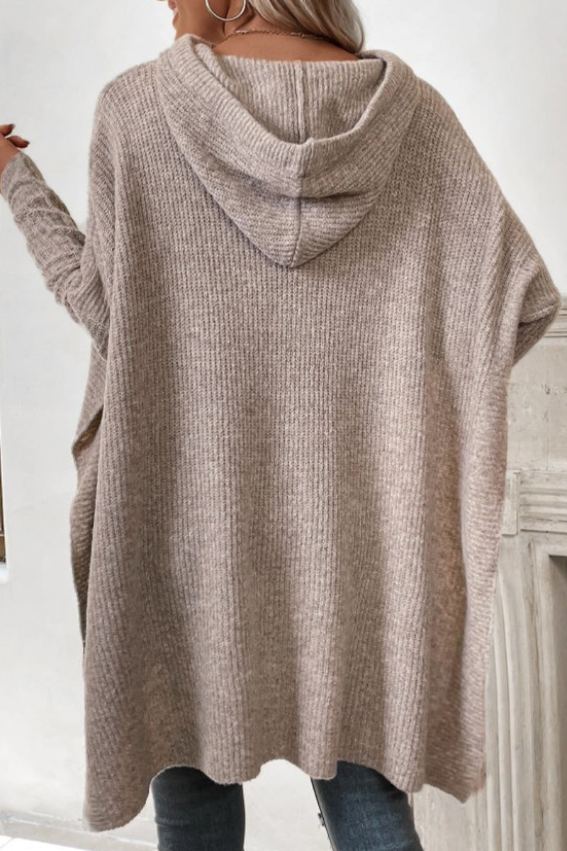 Back view of a woman wearing a beige knit poncho with a hood.