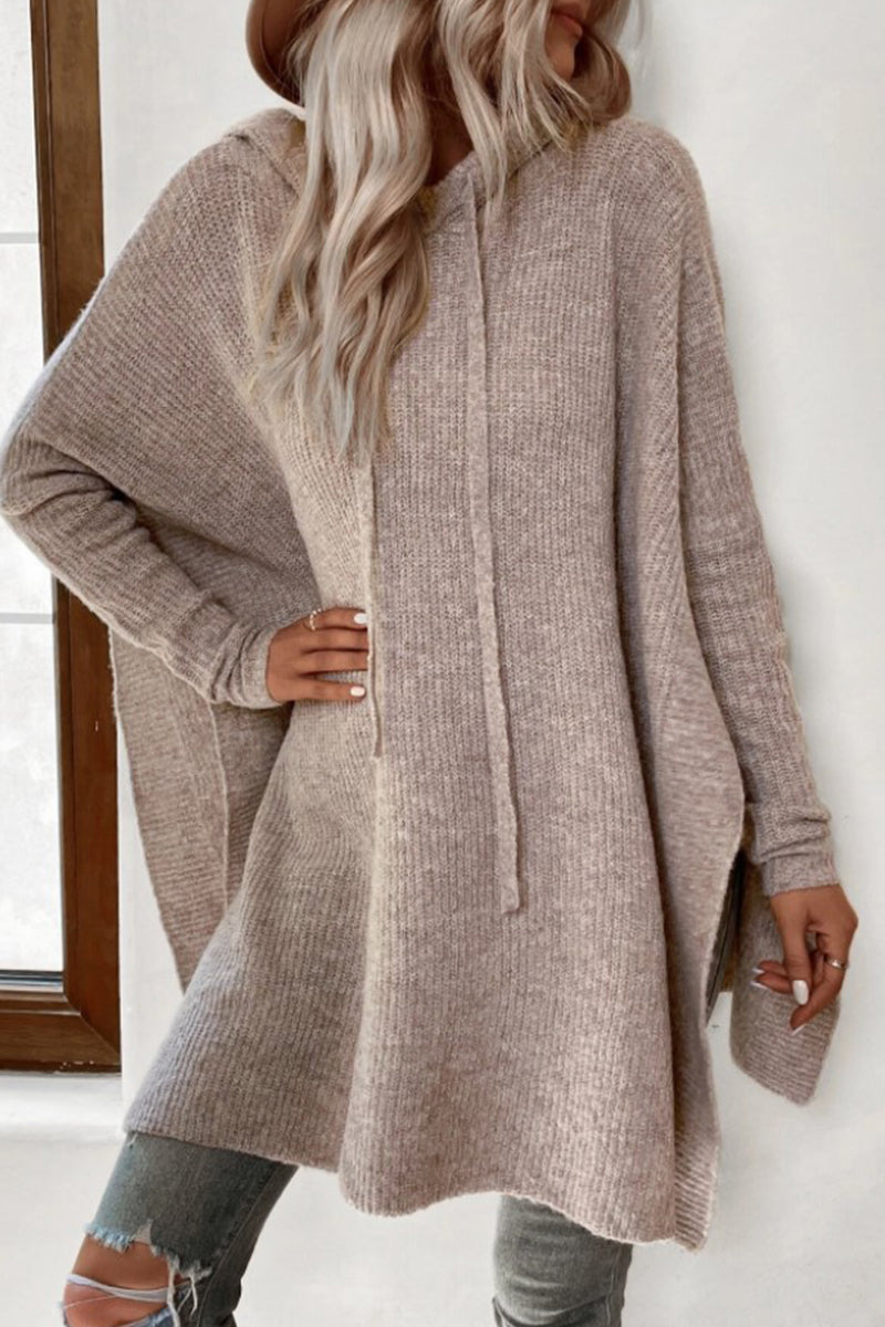 Woman wearing a beige knit poncho with a hood and drawstring, paired with ripped jeans.